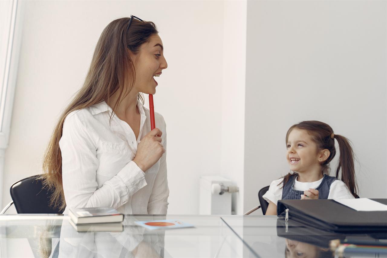 A speech-language pathologist practicing mouth and tongue movements with a smiling young student during a therapy session
