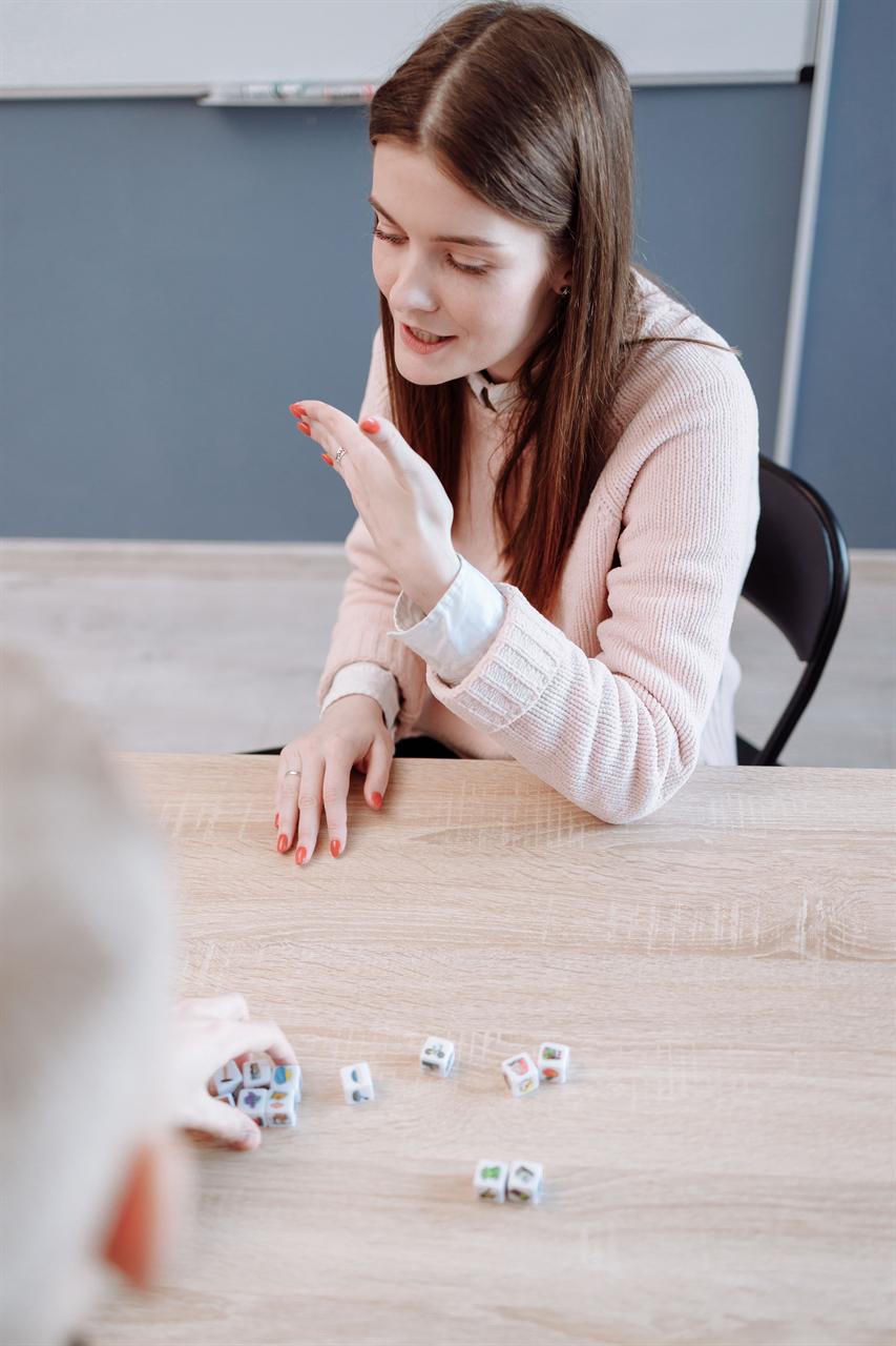 A speech-language pathologist modeling a speech sound while a young student practices with picture cubes at a classroom table