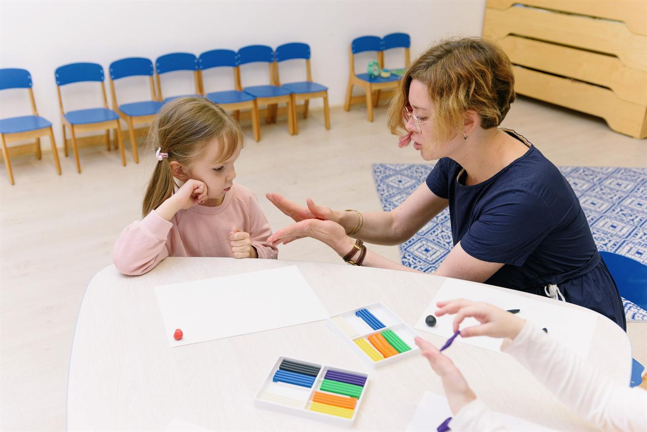 A special education therapist working one-on-one with a young child at a classroom table using colorful learning materials